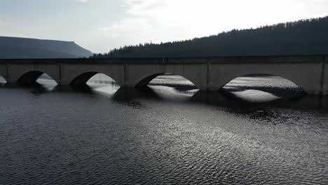 Aeria-drone-flight-under-the-archway-of-the-bridge-at-Ladybower-Reservoir-in-Derwent-Valley-in-the-Peak-District