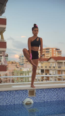 woman practicing yoga by a pool on a rooftop