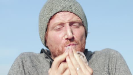 a close shot of the face of a ginger haired man sneezing into a handkerchief and wiping his nose