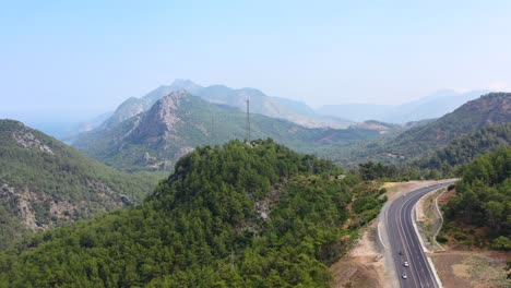 Vista-Panorámica-Aérea-Sobre-Los-Picos-Del-áspero-Paisaje-Montañoso-De-Tauro-Y-La-Carretera-Que-Pasa-Por-El-Valle-Cerca-De-La-Costa-Mediterránea-De-Antalya-Turquía-En-Un-Día-Soleado-De-Verano