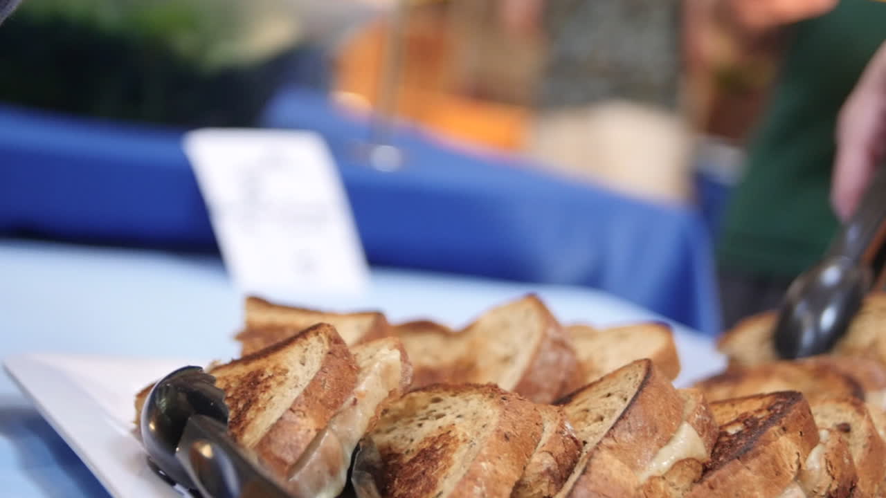 Traveling shot of people serving themselves grilled cheese sandwiches in a cafeteria.