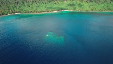 aerial approaching view to boat anchored over underwater cliff in tropical sea by exotic island