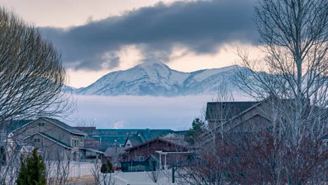 two layers of clouds moving in opposite directions in front of snowy mountains beyond a suburban neighborhood - static time lapse