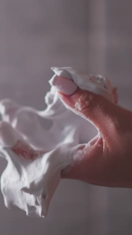 woman squishes body mousse by palm in bathroom closeup. lady hand whips skin care soft foam in shower cabin. organic cosmetic product for spa