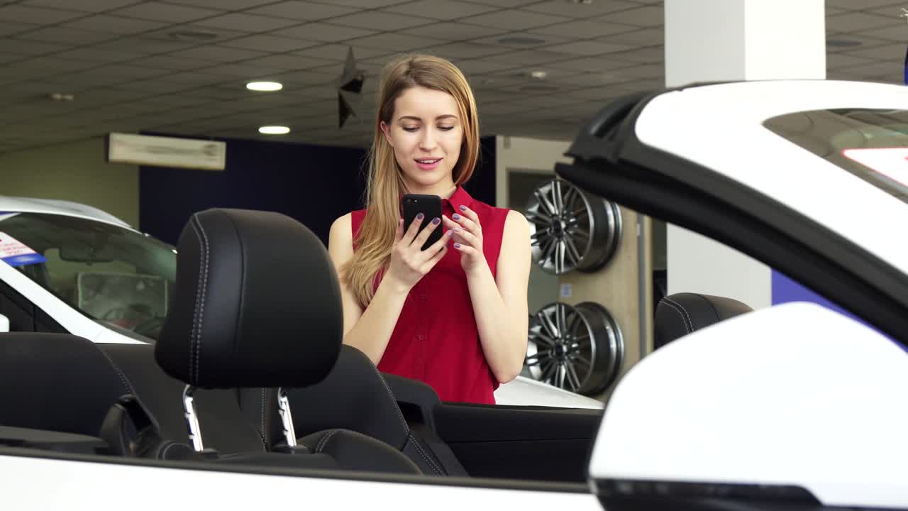 una mujer joven tomando fotos de un nuevo descapotable en el concesionario.