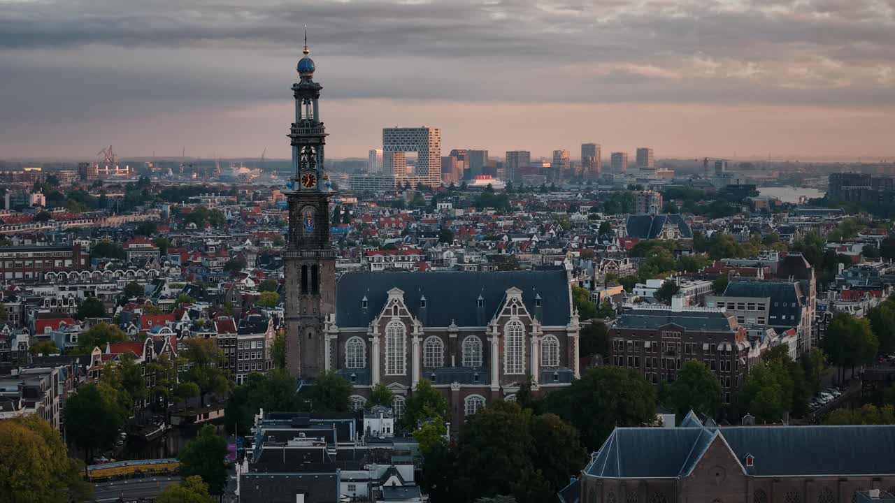 A tall church rises over Amsterdam with twin-tower modern architecture behind