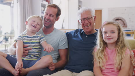 grandfather sitting on sofa with grandchildren and adult son talking and laughing