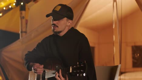 man plays the guitar and sings songs in a tent with light bulbs