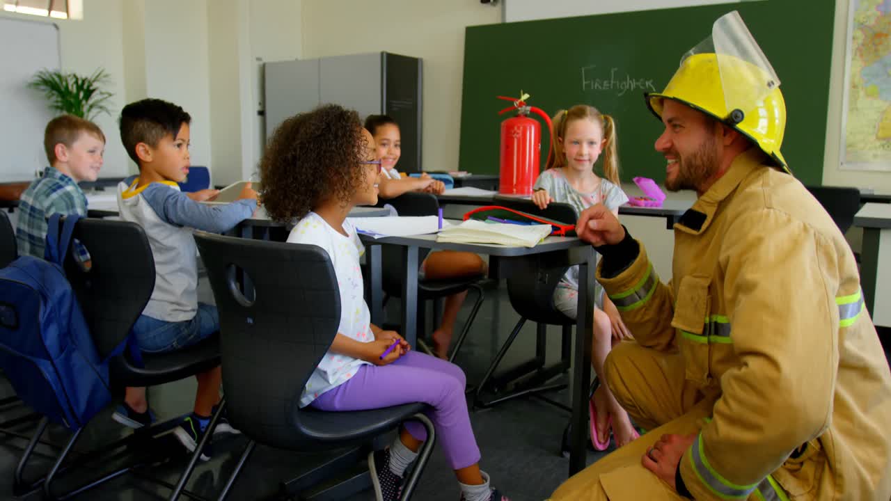 Young handsome Caucasian male firefighter teaching schoolgirl about fire safety in classroom 4k