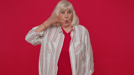 Cheerful-senior-woman-in-shirt-looking-at-camera-doing-phone-gesture-like-says-hey-you-call-me-back