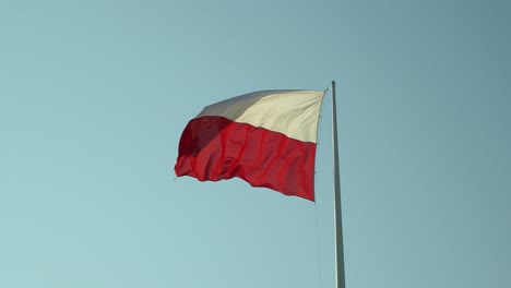 bandera polaca en un mástil, revoloteando en el viento, en un día de cielo azul claro