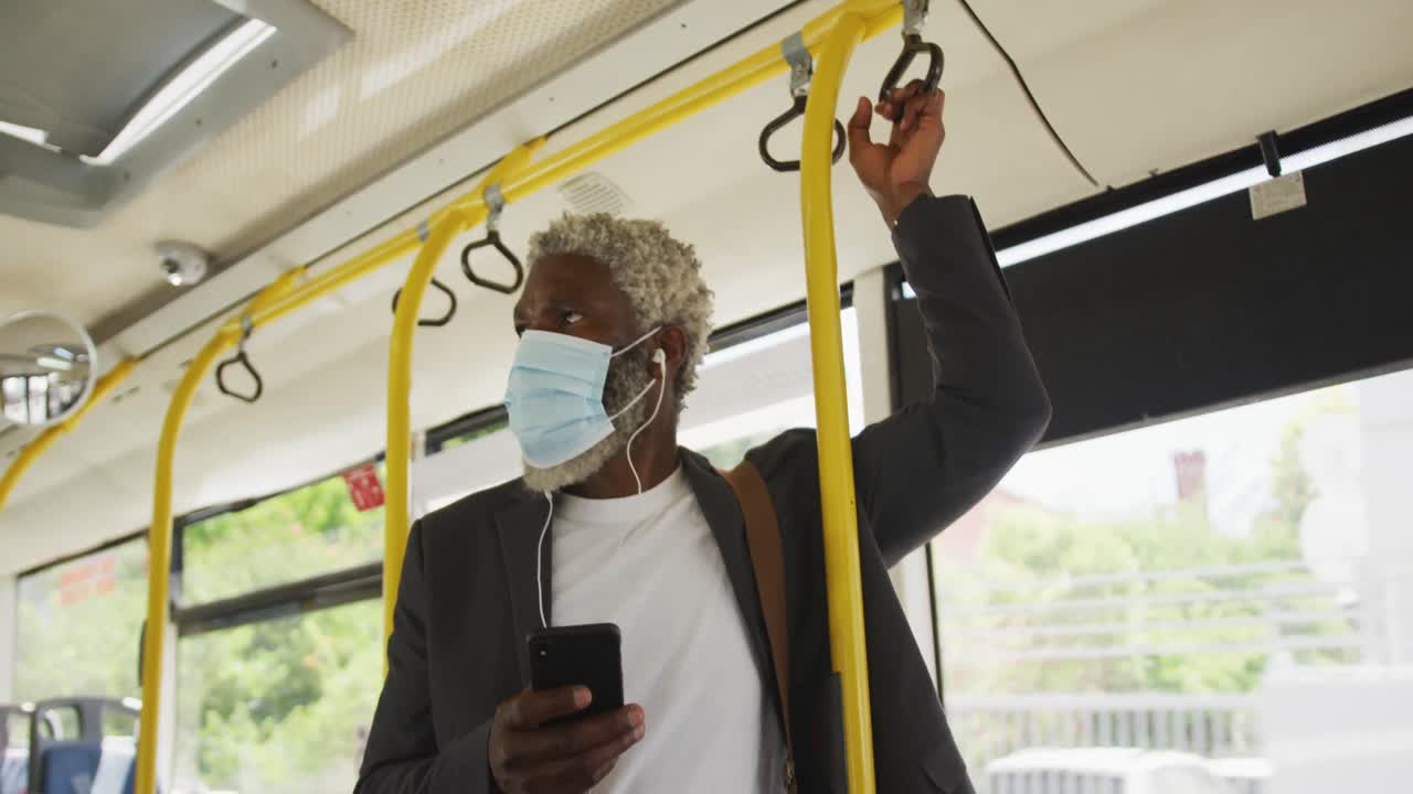 African american senior man wearing face mask using smartphone while standing in the bus