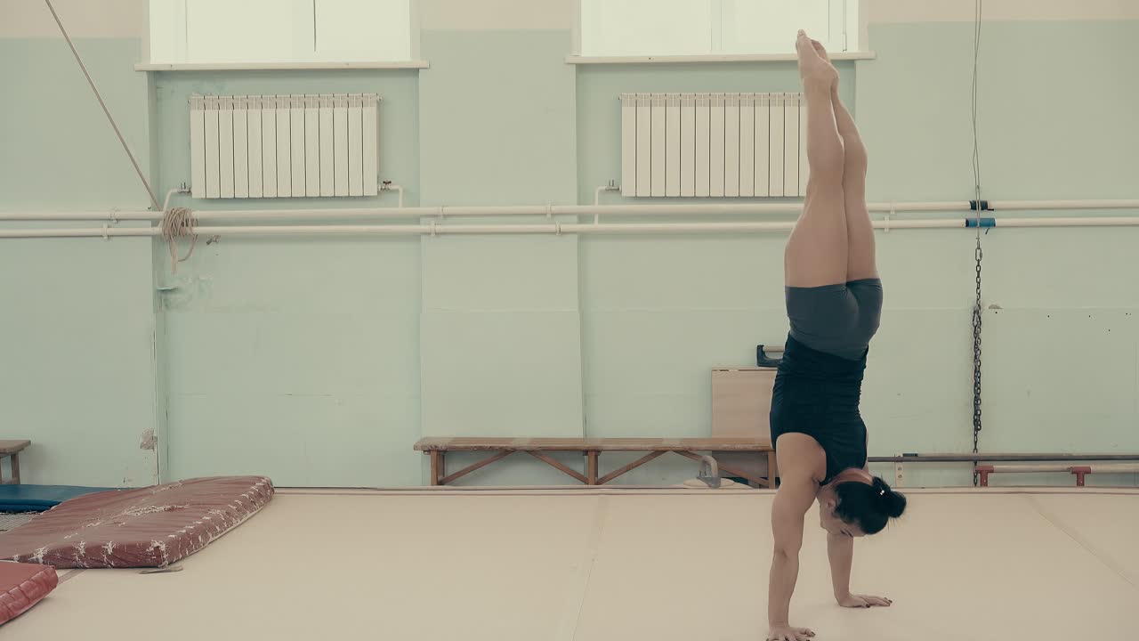 chica atlética en el gimnasio se levanta en sus brazos camina hacia adelante en sus manos girando alrededor de su propio eje