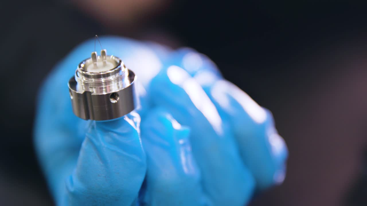 close up of blue gloves holding up microscope piece