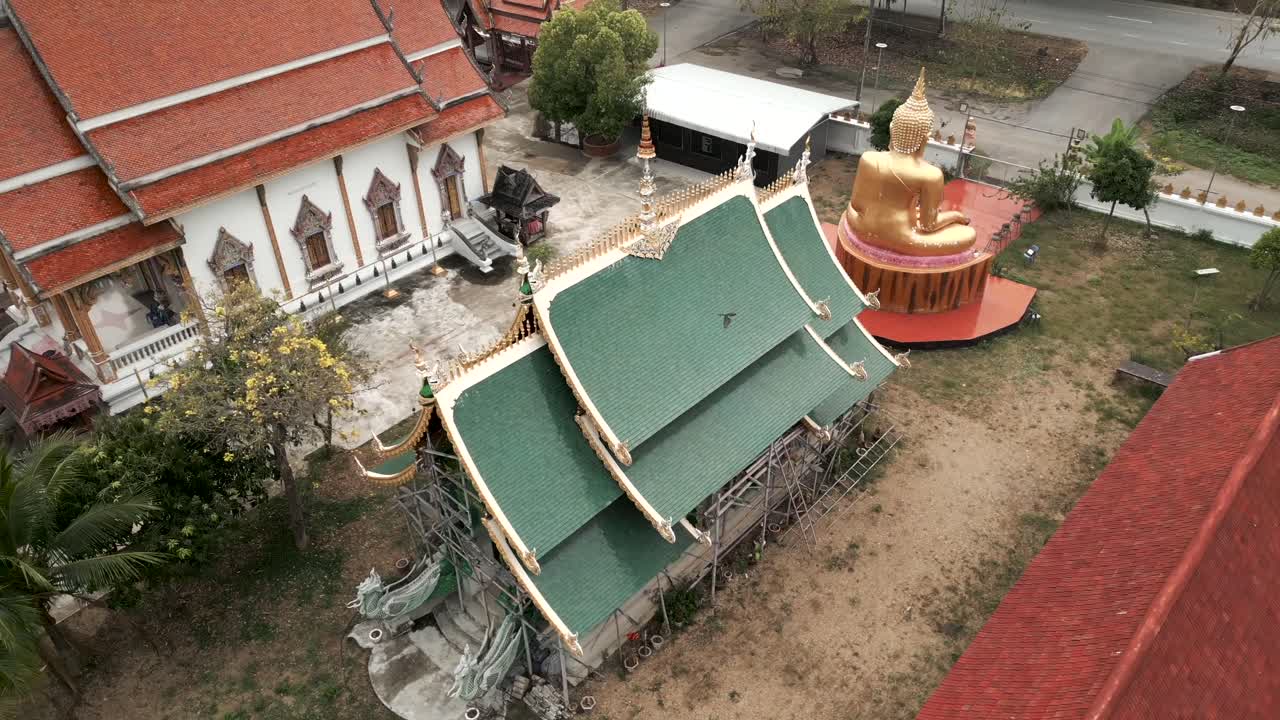 Aerial view of a Buddhist temple complex in Thailand featuring a large golden Buddha statue and traditional buildings