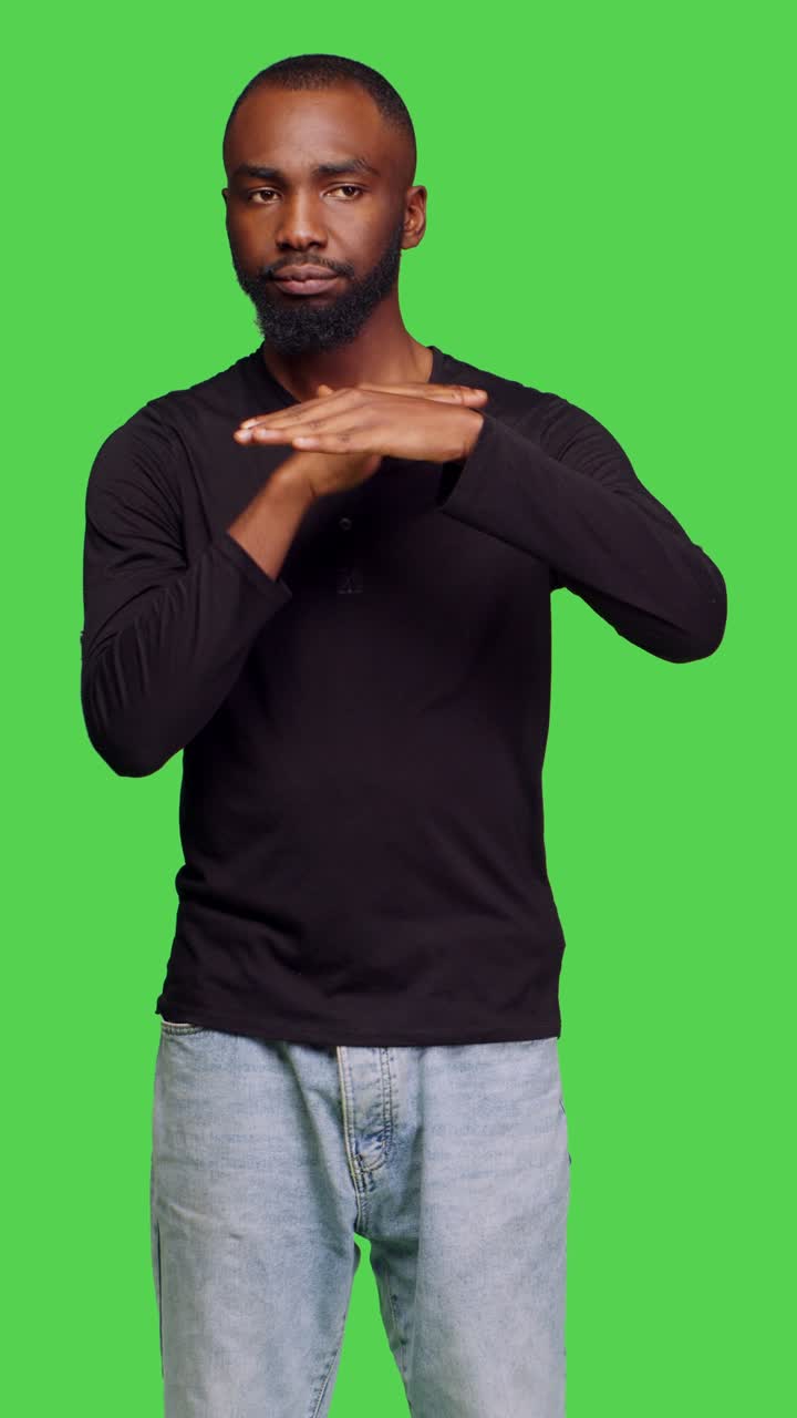 Vertical video: Front view of confident casual man expressing timeout gesture in studio