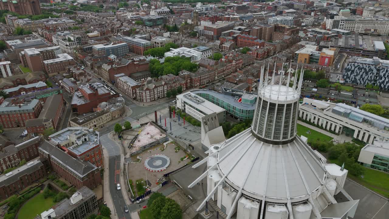 Aerial drone shot circles the iconic modern spire of Liverpool Metropolitan Cathedral, with a panoramic view of the city cityscape in the background. Merseyside, England, UK