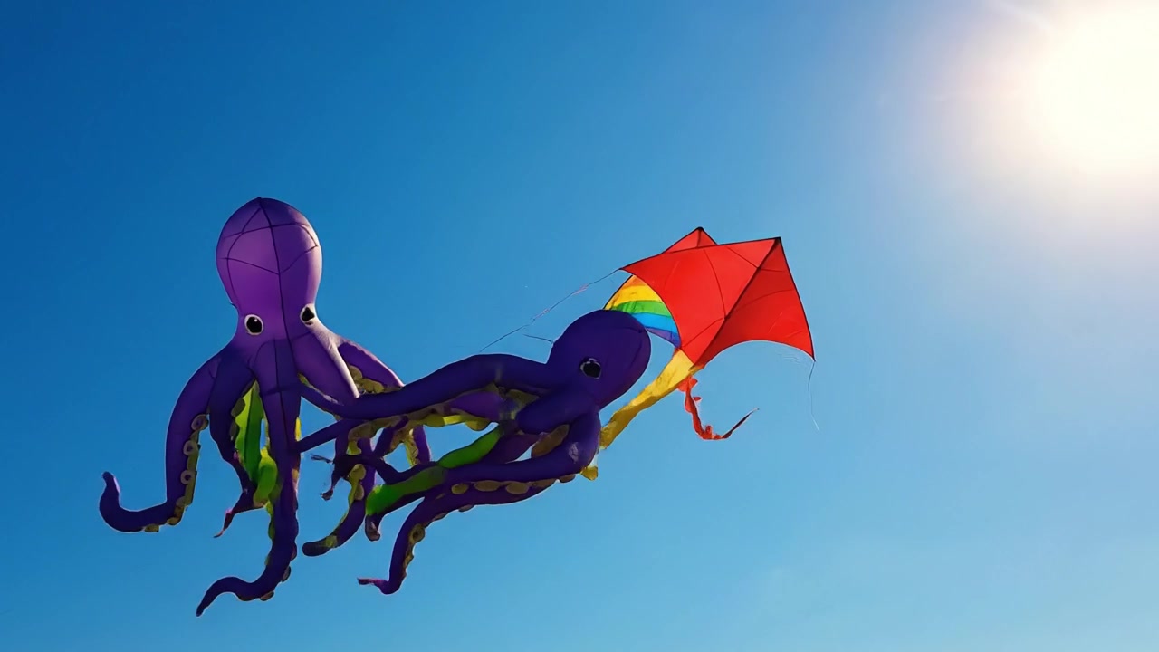 Fargerike drager svever på en klar blå himmel: Et levende skue av livlige design og fantasifulle former som fanger gleden ved utendørs drageflyging
