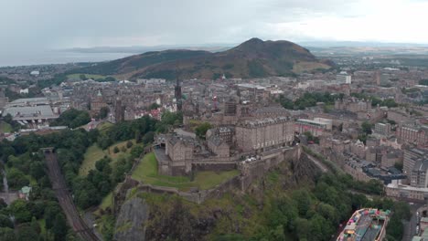 Dolly-forward-pan-down-drone-shot-of-Edinburgh-castle-with-king-arthurs-seat-in-the-background