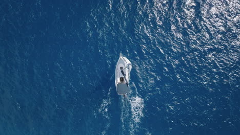 cenital drone shot of a yacht in full sail, riding the waves in the energetic and crystal-clear blue waters, as the wind fills its sails and propels it forward in mexico