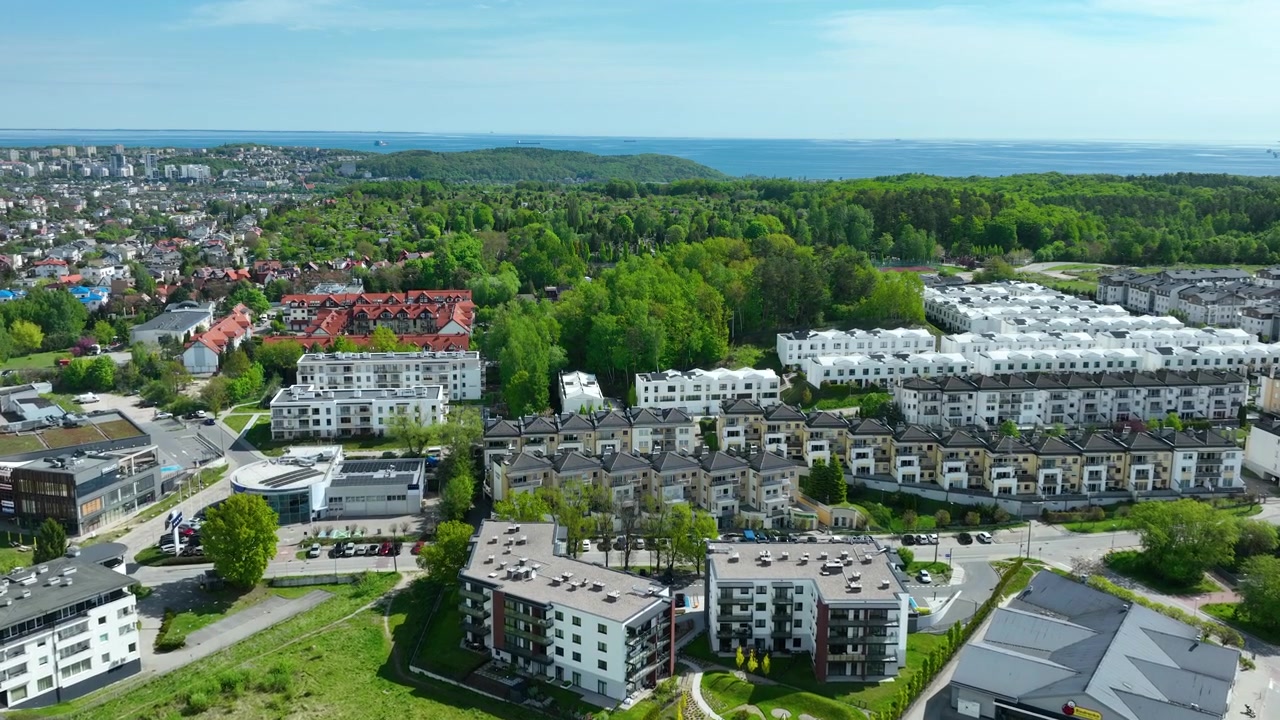 Ufukta deniz manzarası olan yeşil ormanlarla çevrili modern apartman binaları ve banliyö evlerinin yüksek açılı drone çekimi. Emlak ve kentsel gelişim konsepti.