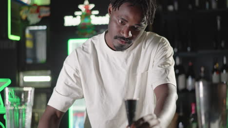 bartender pouring whiskey from bottle into cocktail shaker with focused expression, preparing drink at modern bar with neon lighting in vibrant atmosphere