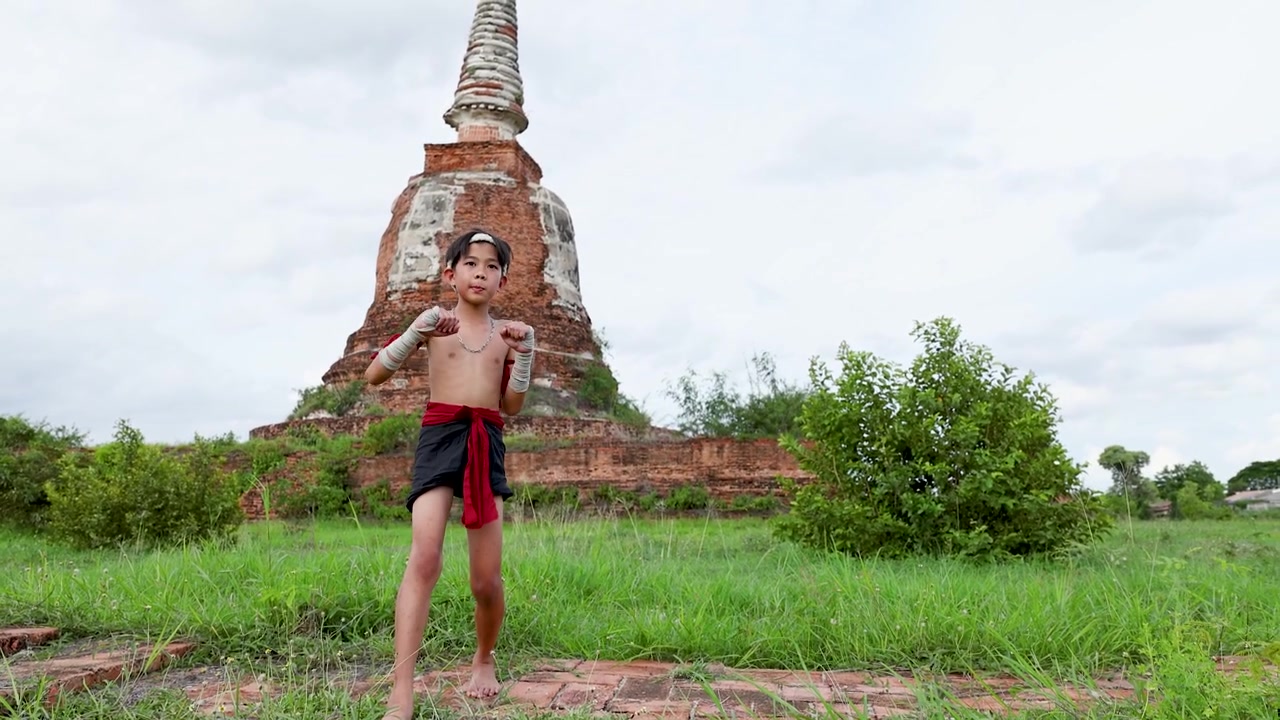 Un niño practica movimientos tradicionales de artes marciales frente a las ruinas de una antigua pagoda de piedra.