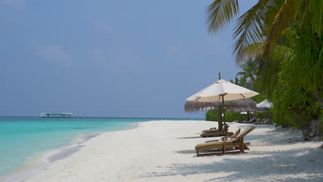 Playa-Tropical-Con-Olas-Suaves,-Palmeras,-Tumbonas-Y-Sombrillas