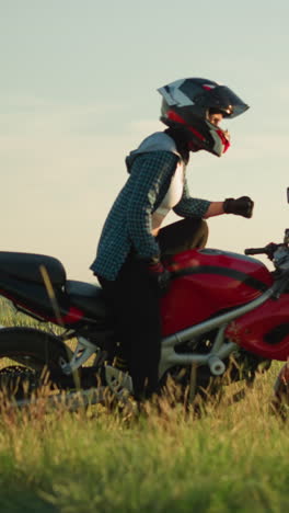 a young woman lies back on a red power bike in an open grassy field with a helmet on, slowly, she raises herself, using her left hand to balance on the motorcycle