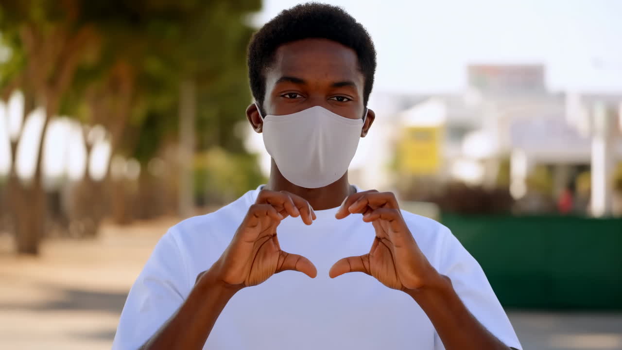Giovane uomo afroamericano con mascherina che fa il gesto del cuore