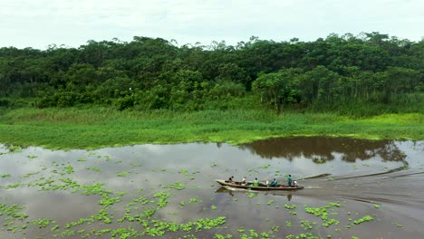 people traveling on amazon river with lush jungle rainforest in background - aerial tracking shot