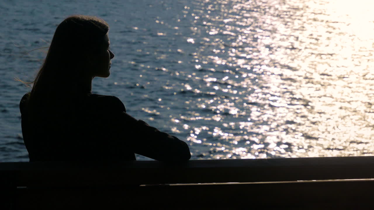 Young pretty professional woman sits and sorrowfully contemplates her thoughts while silhouetted in front of a glimmering lake.