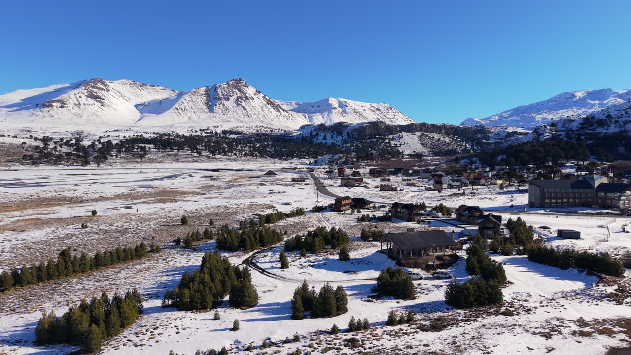 Snow-covered ski resort village of Caviahue, nestled on the shore of a lake at the base of the Andes mountains in Argentina - A beautiful aerial panning reveal