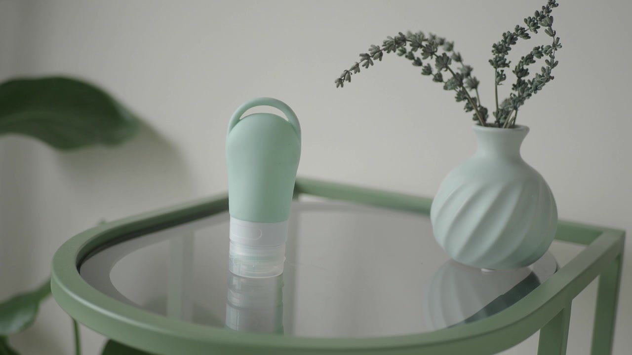 Petite bouteille de voyage verte et vase sur une table en verre