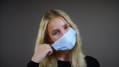 young blonde woman removes face mask smiles