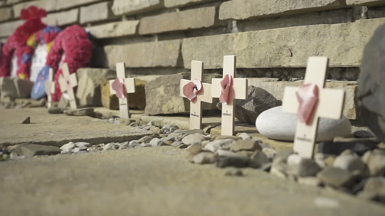 Small wooden crosses with pink hearts and poppy wreaths rest at the base of a brick war memorial