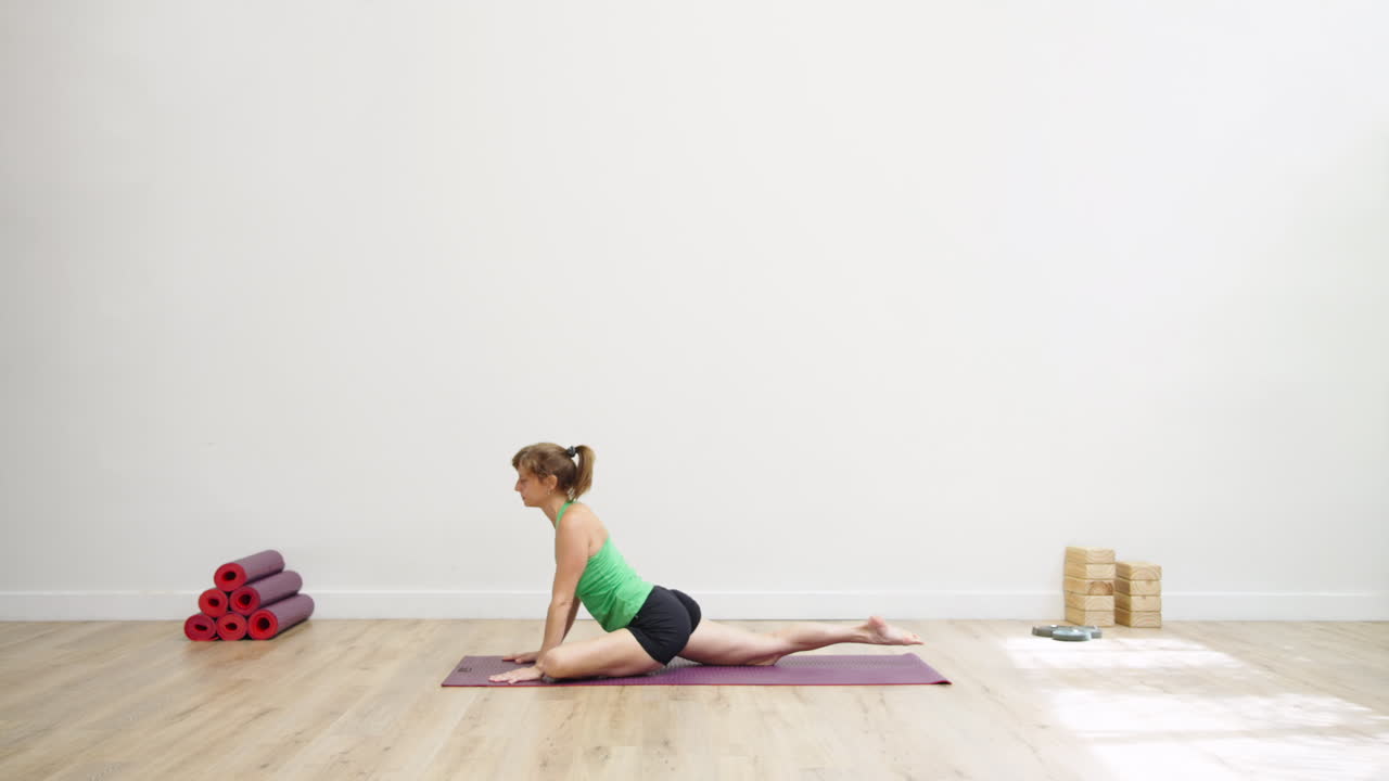 Frau praktiziert Yoga-Posen auf einer Matte in einem hellen Studio