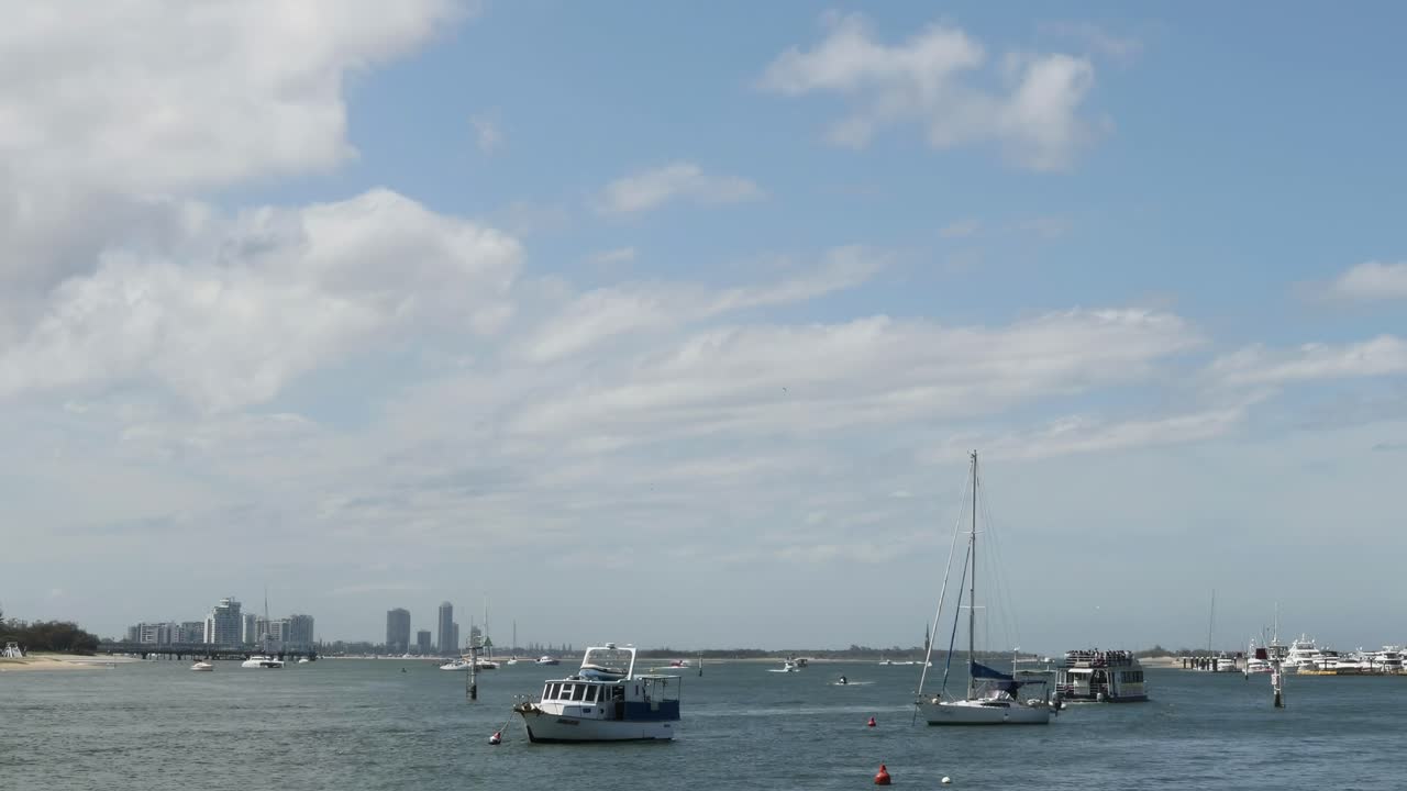 A serene view of boats on the water with a city skyline in the distance under a partly cloudy sky.