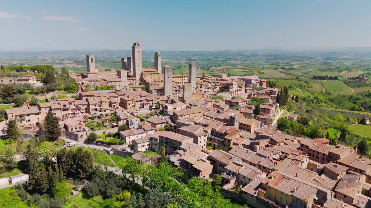 Drone che si solleva e vola indietro su San Gimignano, Toscana, Italia, rivelando altri tetti medievali, torri e le circostanti colline toscane nella morbida luce del mattino