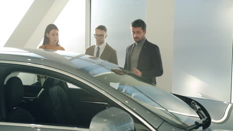 car salesman discussing a vehicle with customers in a showroom