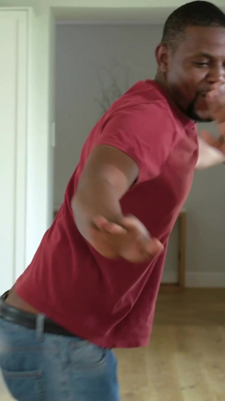 Video verticale: Tenendosi per mano, uomo e donna che ballano per divertimento in cucina vicino a porte scorrevoli, maglietta rossa