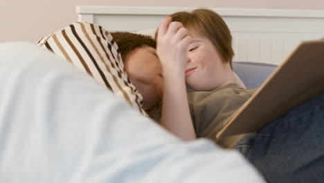 young girl kissing her mother and reading magazine on bed