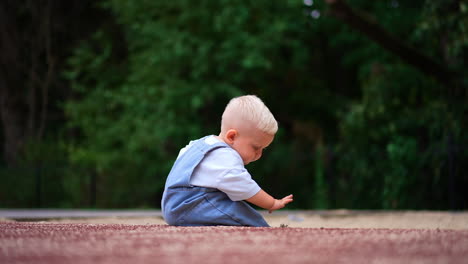 small kid sitting on the ground outdoors. curious kid plays with sand in summer. blurred nature backdrop.