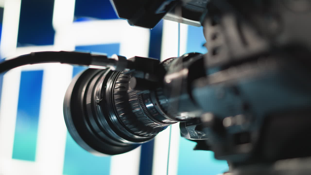 Close up of professional cinema camera lens with focus rings reflecting blue green studio lights, showcasing internal glass elements, textures and optical coatings for broadcast filmmaking detail shot