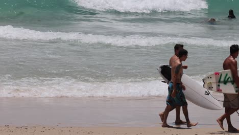 group of surfers carrying boards on a sandy beach