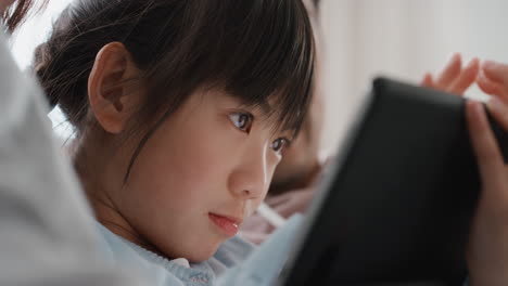 little asian girl using tablet computer watching entertainment with parents playing game on touchscreen device browsing online relaxing on sofa together at home 4k