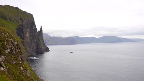 Aerial-wide-shot-of-Trollkonufingur-and-stunning-mountainous-landscape-with-steep-cliff-at-Atlantic-Ocean