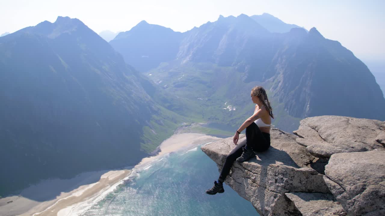 mujer atractiva con cabello trenzado sentada sobre una cornisa de roca con vistas al mar.