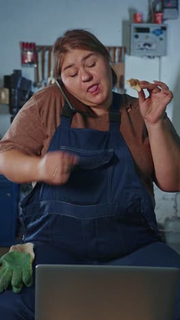 woman mechanic eating while working on laptop and talking on phone