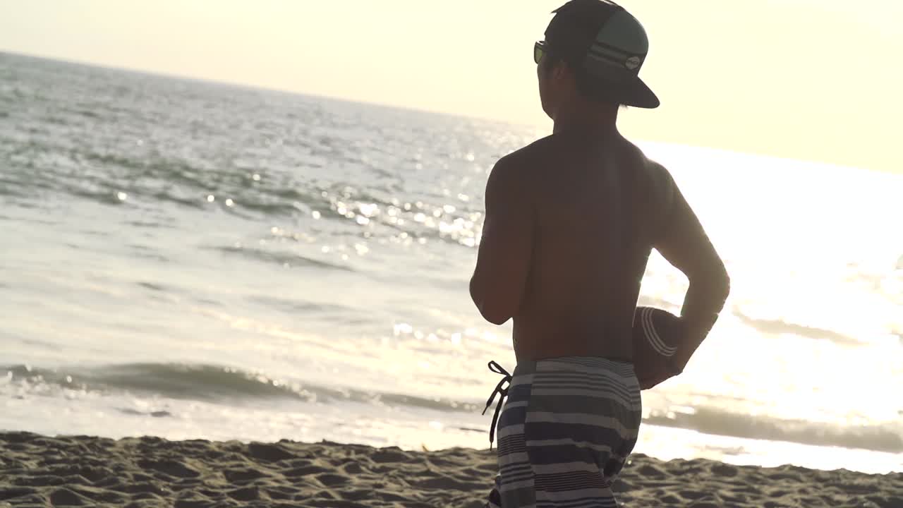 Kid running with football in slow motion on the beach during sunset in California